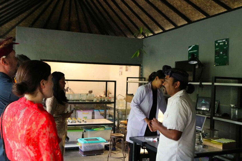 A group of people in a laboratory setting with shelves containing glassware and equipment. 2
