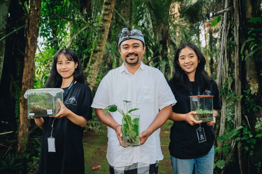 Three individuals holding terrariums in a forested area. 1