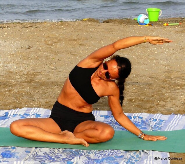 A person performing a yoga pose on a mat at the beach. 1