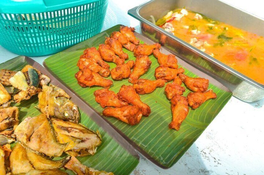 A variety of fried fish and chicken on banana leaves, with a basket and a metal tray in the background. 4
