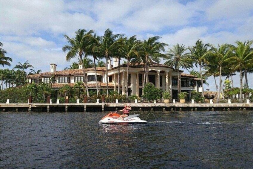 A large house with a waterway in front, a jet ski, and palm trees. 3