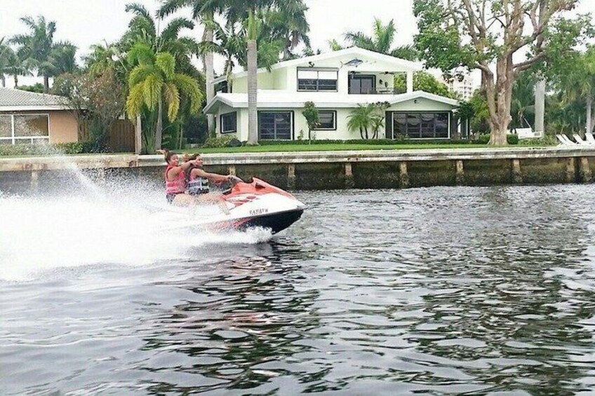 A jet ski on water with a house and palm trees in the background. 2
