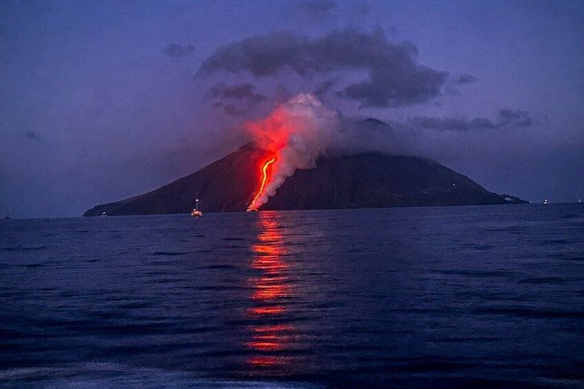 A volcano erupting with lava flowing down its side, a boat in the foreground, and a calm sea reflecting the scene. 1