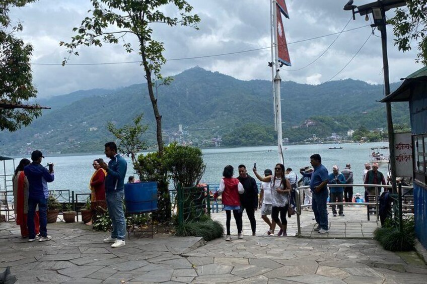 A group of people standing on a stone-paved area by a lake with mountains in the background. 2