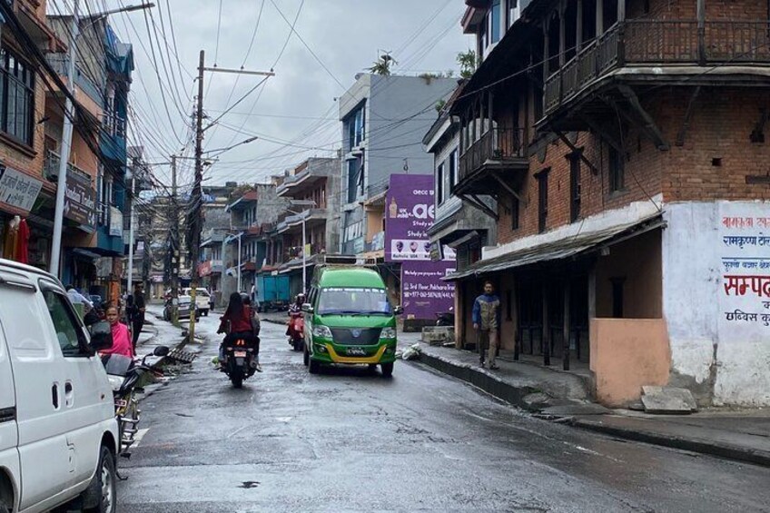 A wet urban street with vehicles, buildings, and overhead power lines. 1