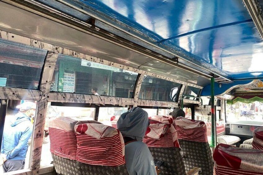 A bus interior with passengers seated, covered seats, and a blue ceiling. 3