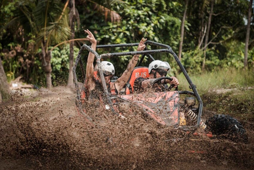 A muddy off-road vehicle with two people, one driving and one passenger, splashing mud. 1
