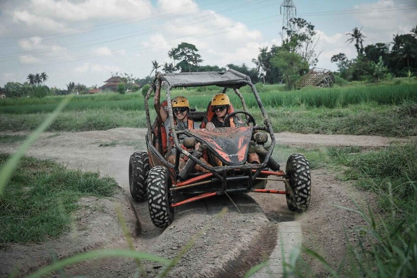 Two people in a four-wheeled vehicle on a dirt road surrounded by greenery. 2