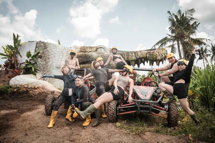 A group of people in outdoor gear posing around a vehicle with a large, dinosaur-like sculpture in the background. 4