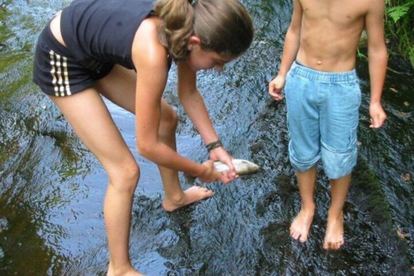 Two people in a shallow stream, one bending over to touch the water. 2