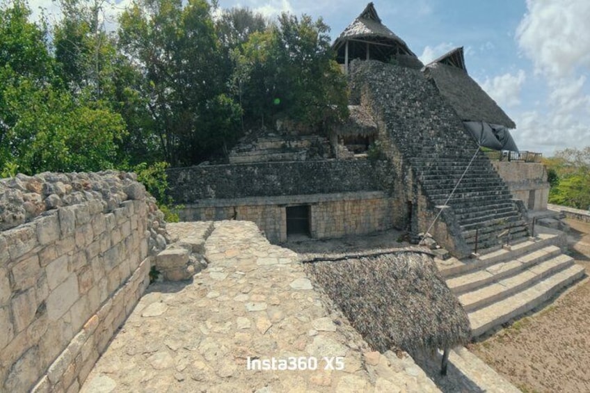 An ancient stone structure with a thatched roof and a staircase leading to a higher platform. 1