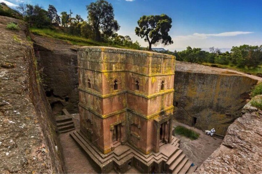 An ancient stone structure with a staircase leading up to it, surrounded by greenery and a clear sky. 2