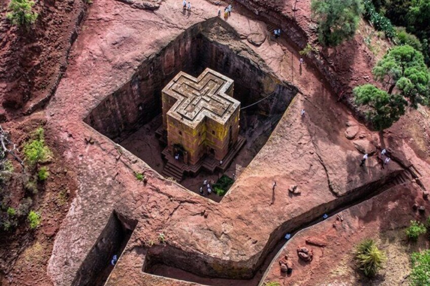An ancient, square-shaped structure with a stepped entrance, surrounded by red rock formations and sparse vegetation. 1