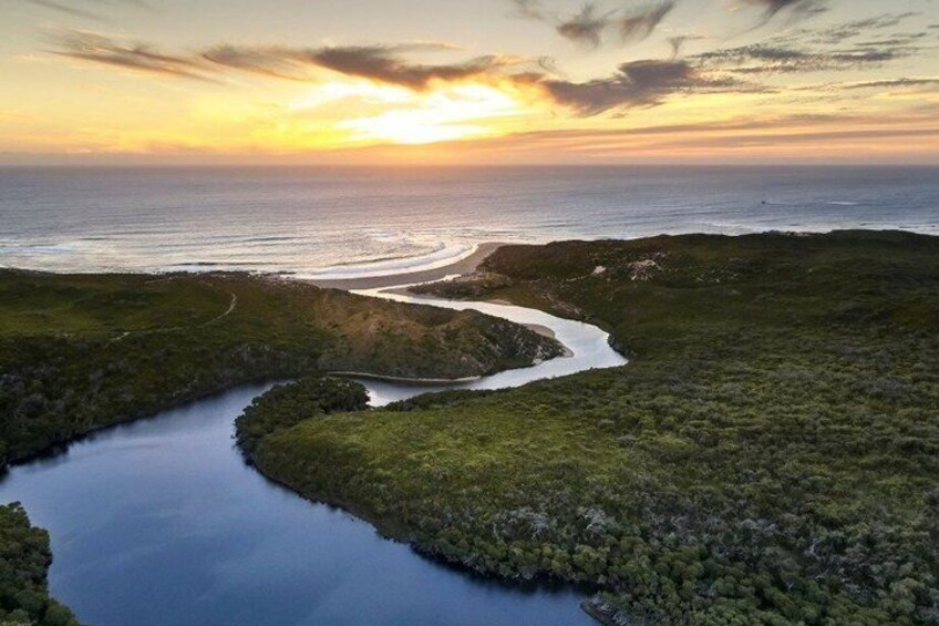 A river winding through a coastal landscape with a sunset in the background. 1