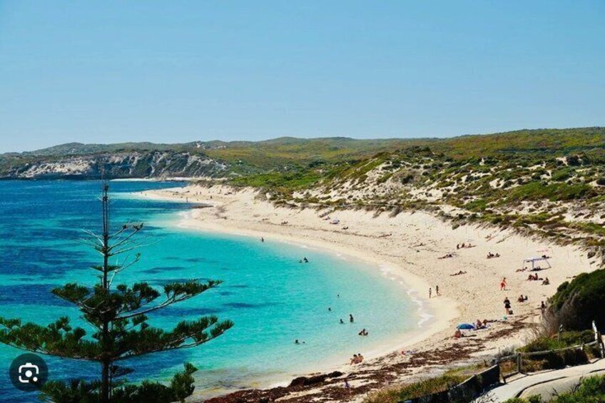 A beach with clear turquoise water, sandy shore, and sparse vegetation. 2
