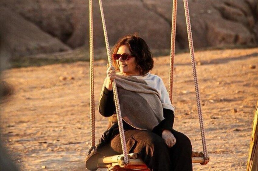 A person sitting on a swing in a desert landscape. 1