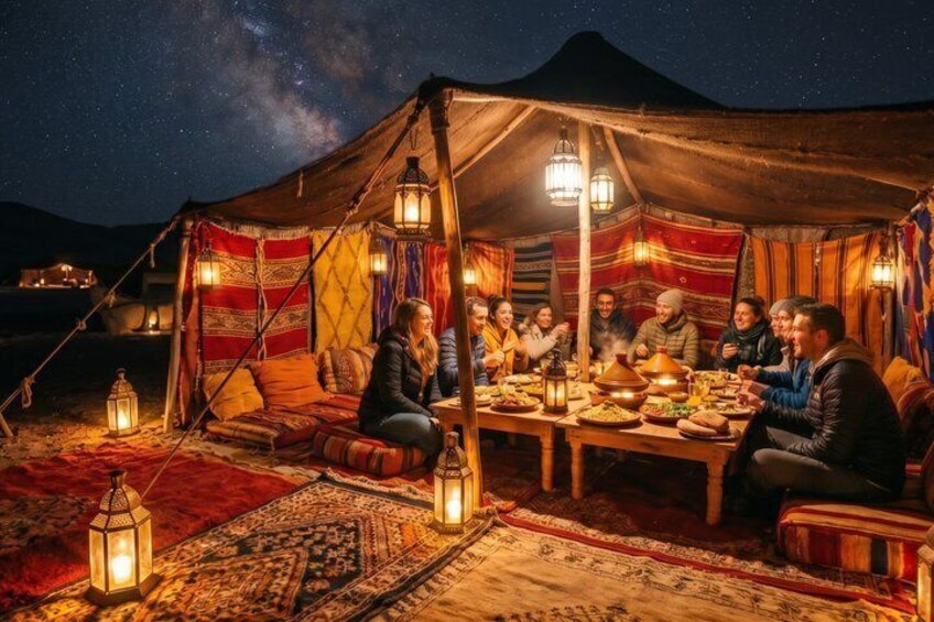 A group of people dining under a tent with lanterns, set against a mountainous backdrop. 1