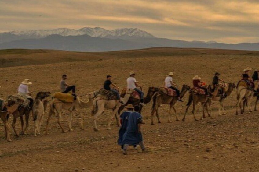 A group of people riding camels in a desert landscape with mountains in the background. 4