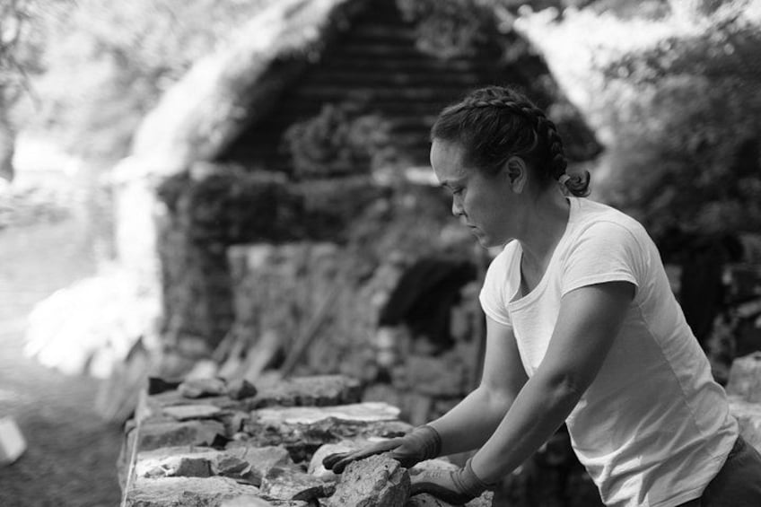A person working with bricks in an outdoor setting with a stone structure in the background. 1