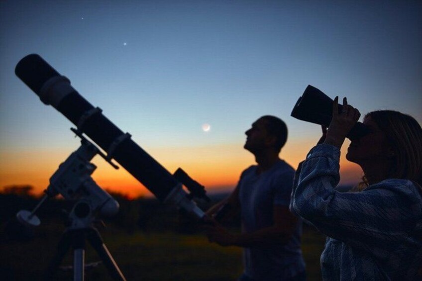 Two people using telescopes at dusk with a moon visible in the sky. 3