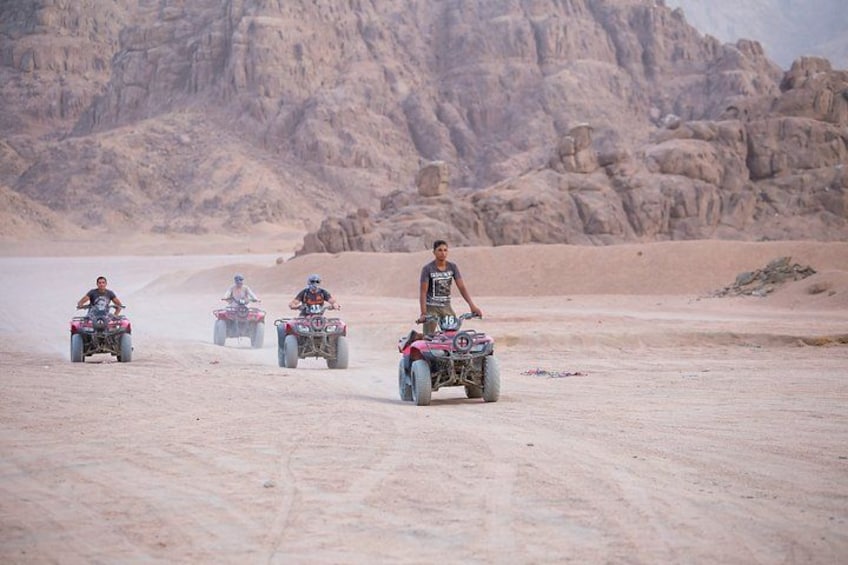 Four off-road vehicles on a desert terrain with rocky mountains in the background. 3