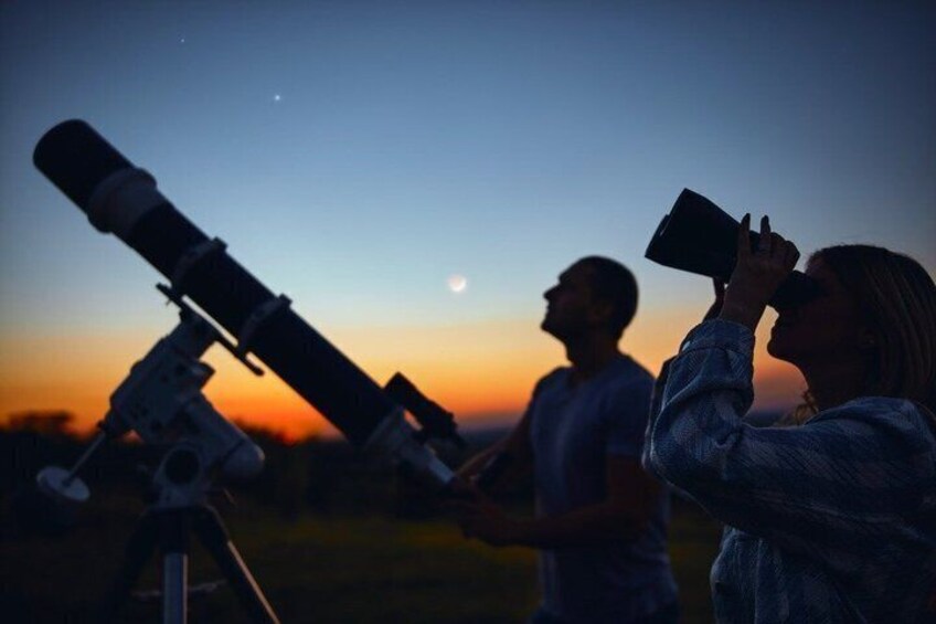 Two people using telescopes at dusk with a moon and stars in the sky. 4