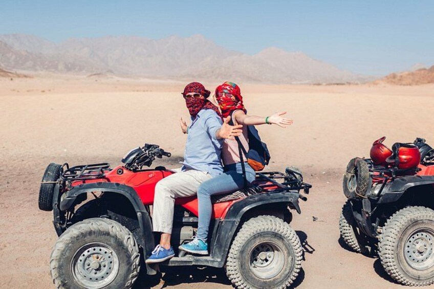 Two people on an ATV in a desert with mountains in the background. 2