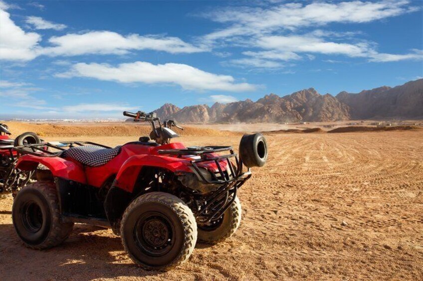 A red ATV parked on a desert with mountains in the background. 1