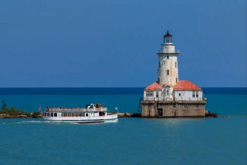 A white boat with passengers, a lighthouse, and calm blue waters. 2