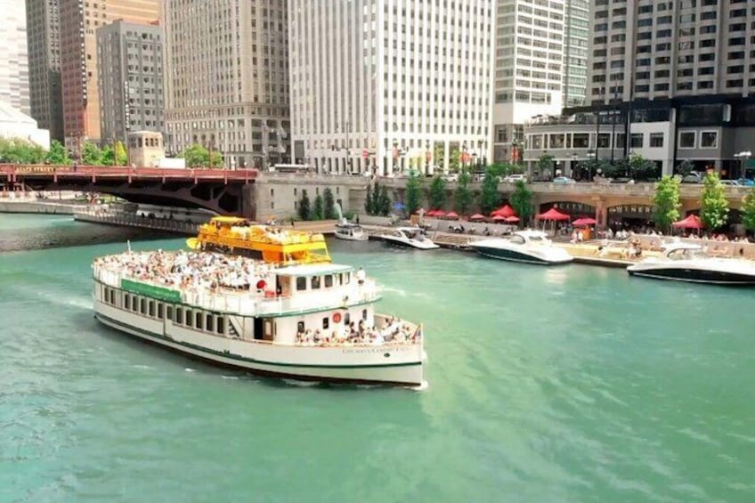 A river with a large boat carrying passengers, surrounded by tall buildings and a bridge. 1