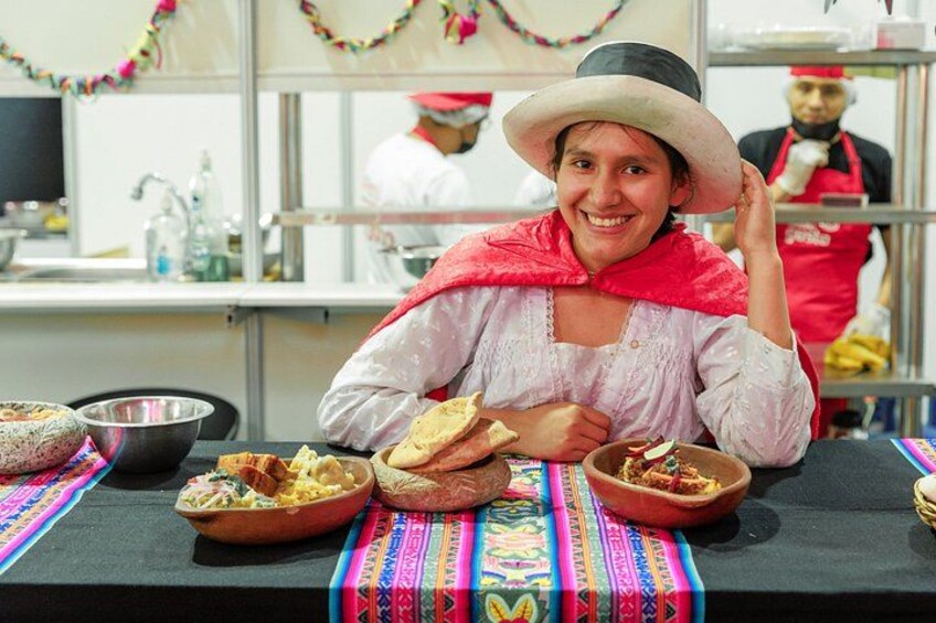 A person in traditional attire sitting at a table with various dishes, a kitchen setting in the background, and a colorful tablecloth. 1