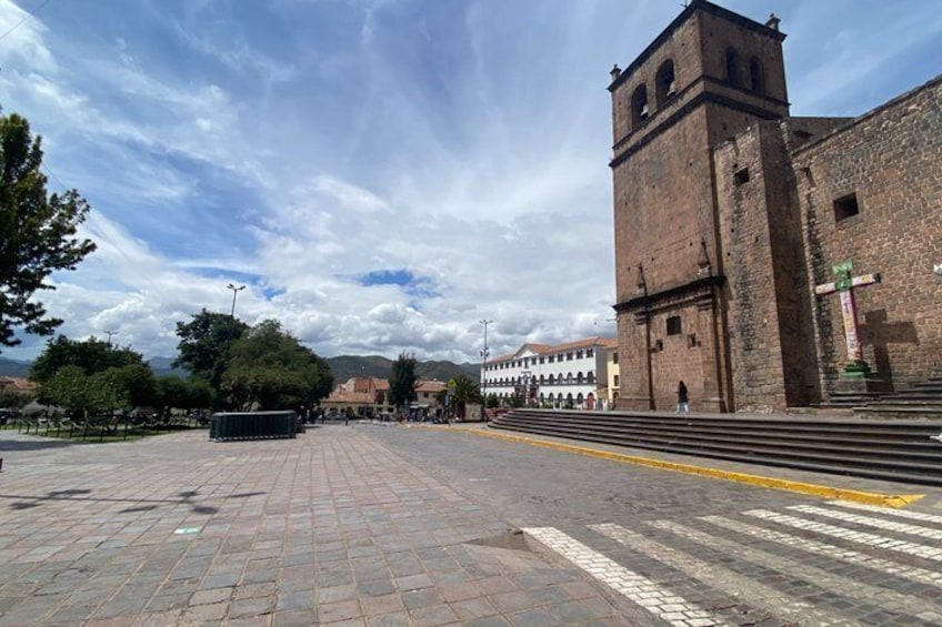 A paved square with a historic building featuring a bell tower, surrounded by trees and a clear sky. 4
