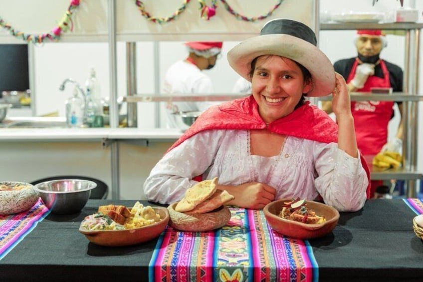 A person seated at a table with traditional dishes, wearing a hat and a red shawl. 1