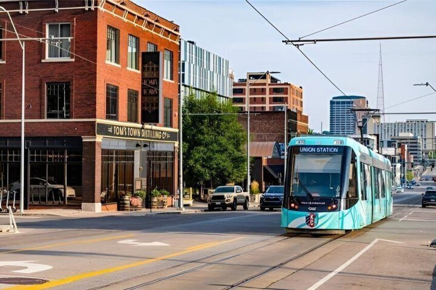 A tram at Union Station, a brick building with 'Tomtown Distilling Co' signage, and modern buildings in the background. 2