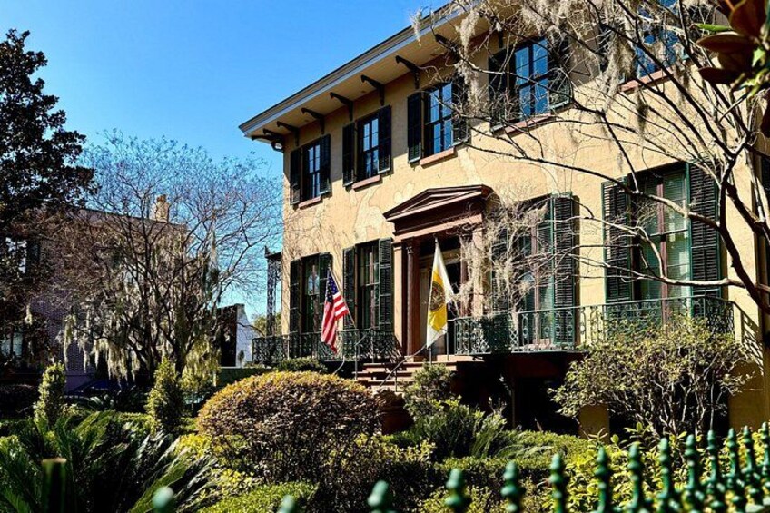 A two-story house with a balcony, a flag, and a well-maintained garden. 3
