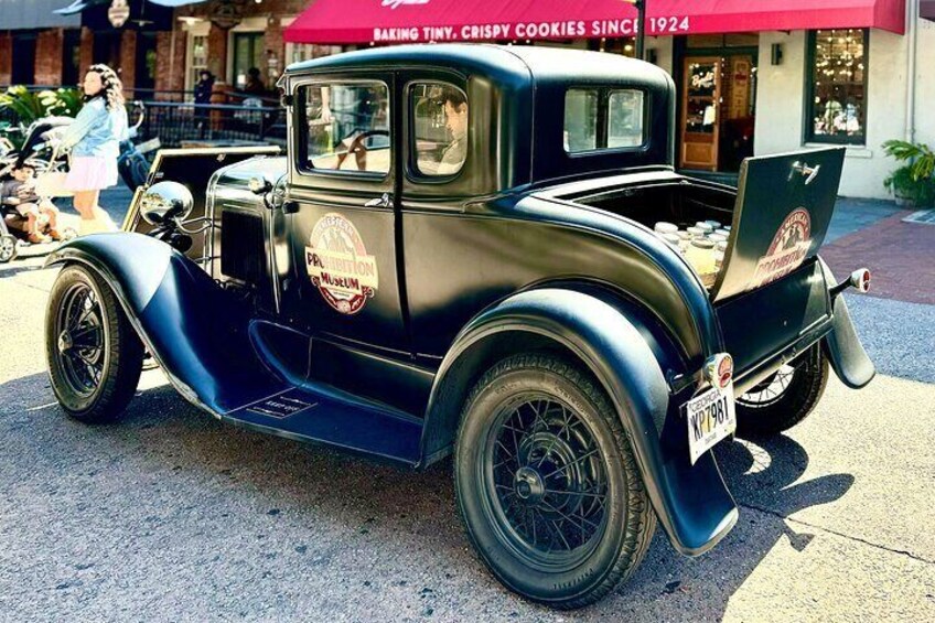 A vintage black car with a license plate, parked on a street. 4