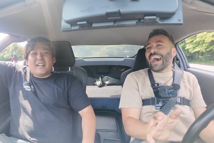 Two people in a car, one driving and one passenger, with a camera strap visible. 1