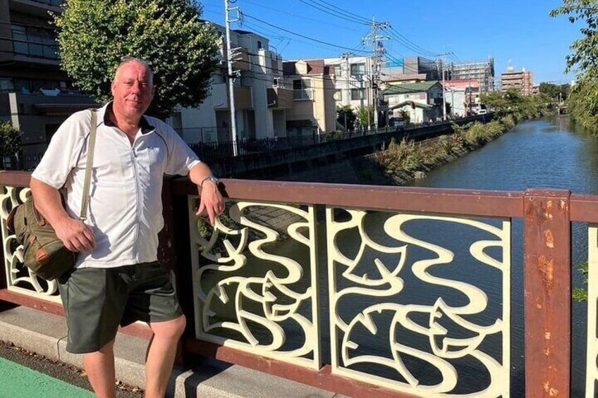 A man standing on a bridge with a river and buildings in the background. 5