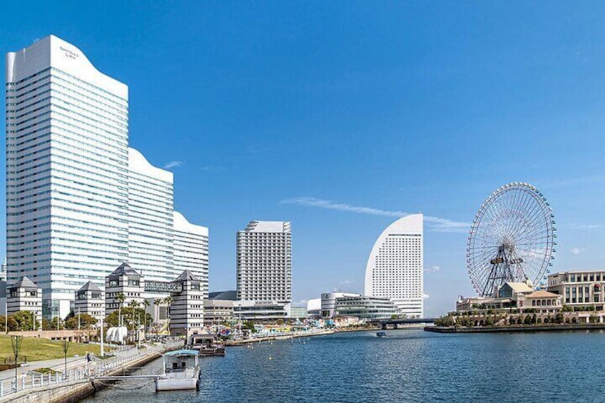 A waterfront cityscape with modern buildings, a Ferris wheel, and a boat docked by the pier. 2