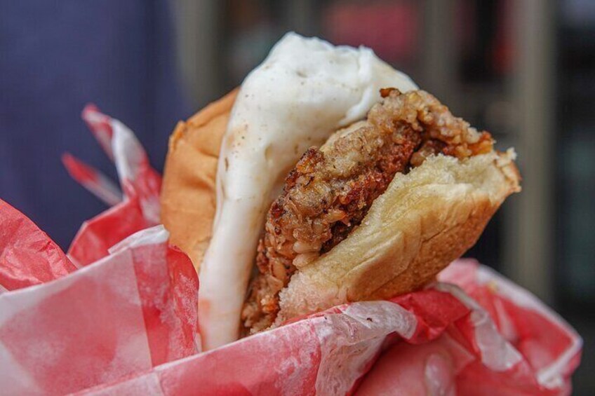 A sandwich with a crispy chicken patty and a white sauce, served in a paper container. 4