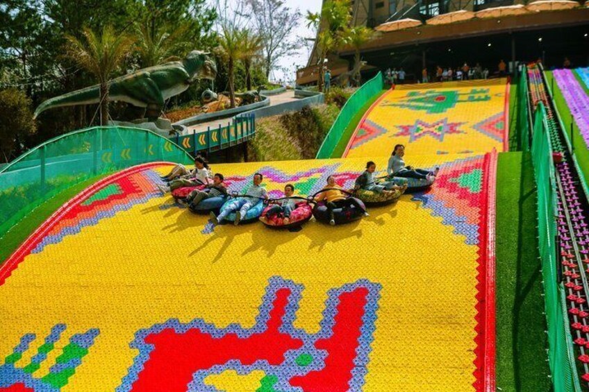 A colorful slide with people at the top, surrounded by greenery and a building in the background. 5