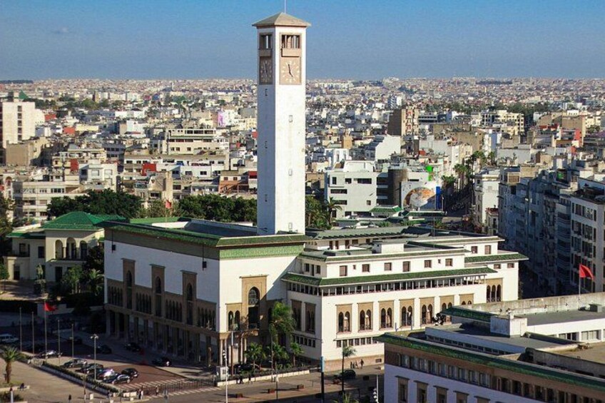 A cityscape with a prominent clock tower, a large building with a green roof, and a densely packed urban area in the background. 2