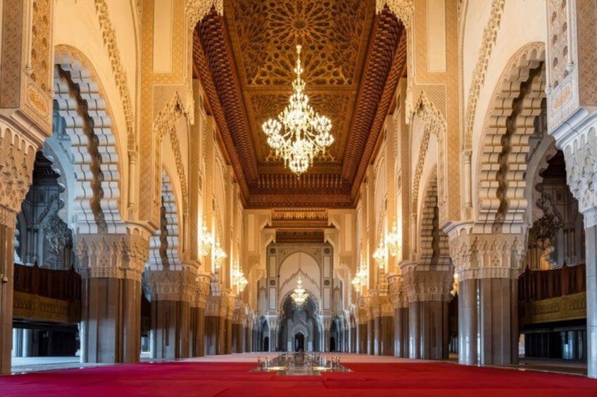 An ornate interior with a red carpet, intricate arches, and a chandelier. 1