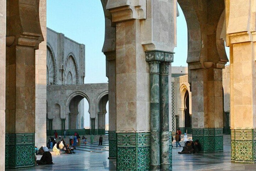 An architectural courtyard with arches and columns, a tiled floor, and people sitting and walking. 2