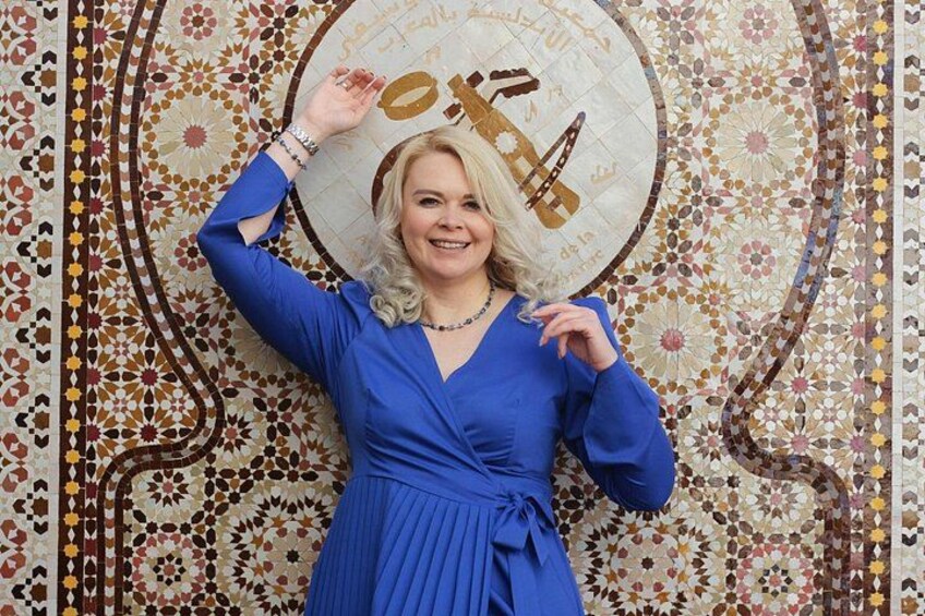 A person in a blue dress standing in front of a patterned wall. 4