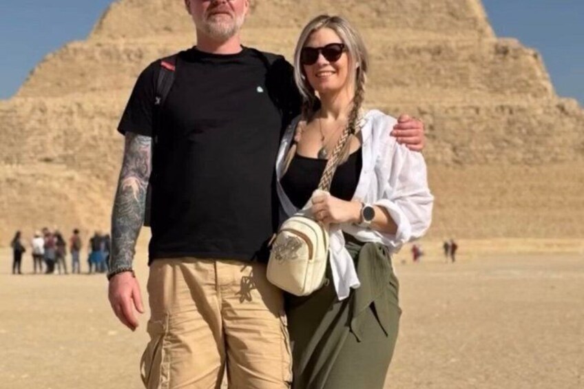 Two people standing in front of a pyramid with tourists in the background. 3