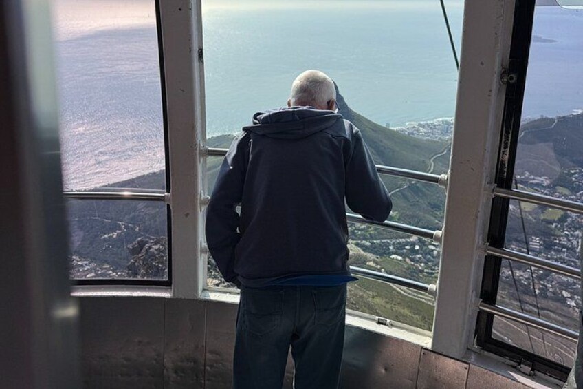 A person standing inside a structure with large windows overlooking a coastal landscape. 2