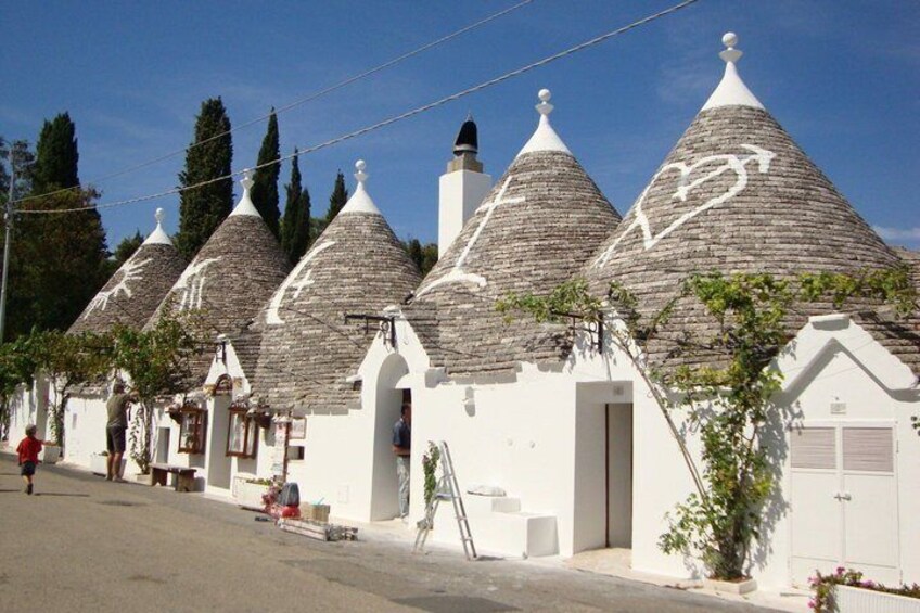 A row of white buildings with conical roofs, a clear blue sky, and a person walking on the street. 1