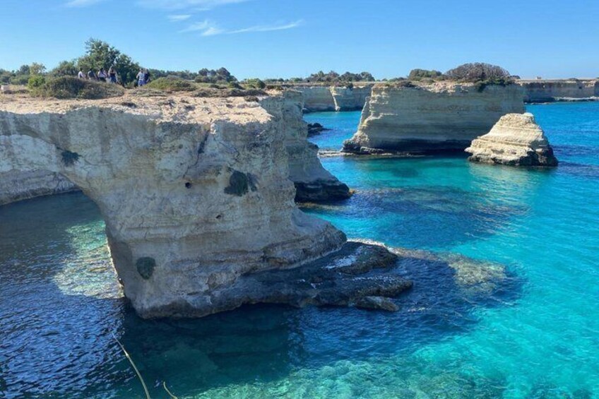 A coastal landscape with clear turquoise waters and prominent rock formations. 1