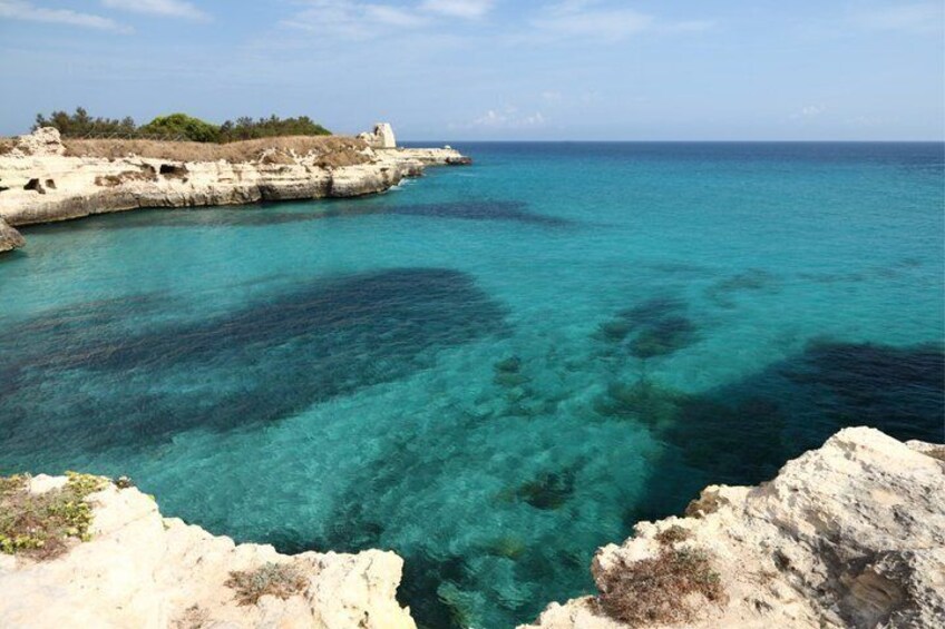 A coastal landscape with clear turquoise waters, rocky cliffs, and sparse vegetation. 2